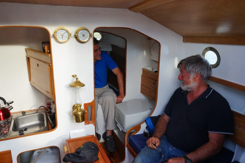 Designer John Welsford (right) pays a visit aboard WHIO. The view looking forward takes in the galley and the portable head head tucked in the passageway to the forward berth.