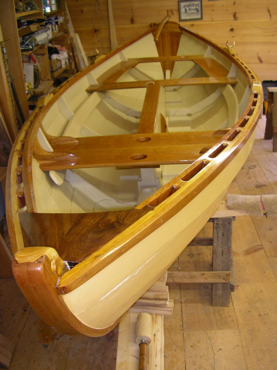 Ready for the water. Gleaming under the varnish is cherry (false stem, thwarts, gunwales), black walnut (Juglans nigra) (breasthook), black locust (Robinia pseudoacacia) (oarlock pads), and apple (knees). Note the two holes at the mast-partners – the mast can be shifted fore or aft depending on the boat load.