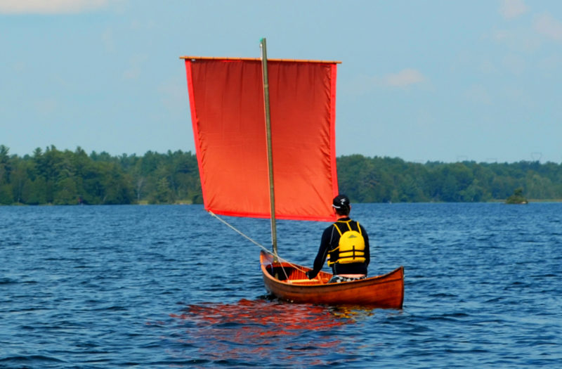 Mike, seated aft and on a broad reach, steering with sheets attached to the lower corners of the sail. A bit of belly or camber in the sail increases its stability, so he has pulled its foot up against the mast and the corners to the rear.
