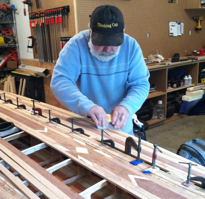 Clamping strips in place avoids the holes left by nails, but slows the work. Capt. Jack uses the time needed for the glue to cure to smooth other sections of the hull.