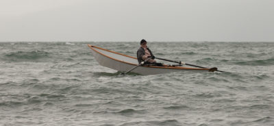 Author Dale McKinnon, in her sliding-seat equipped light dory, makes her way into a headwind and waves,