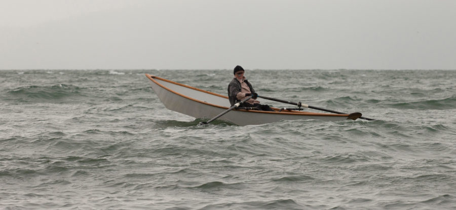 Author Dale McKinnon, in her sliding-seat equipped light dory, makes her way into a headwind and waves,