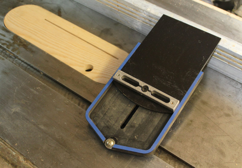 The bottom of the jig has a metal bar that fits and locks in the table saw's miter track. The ball bearing reduces friction as the wood being sawn is pushed by the jig. The zero-clearance jig shown here is made of ash and is splined at the ends to prevent splitting.