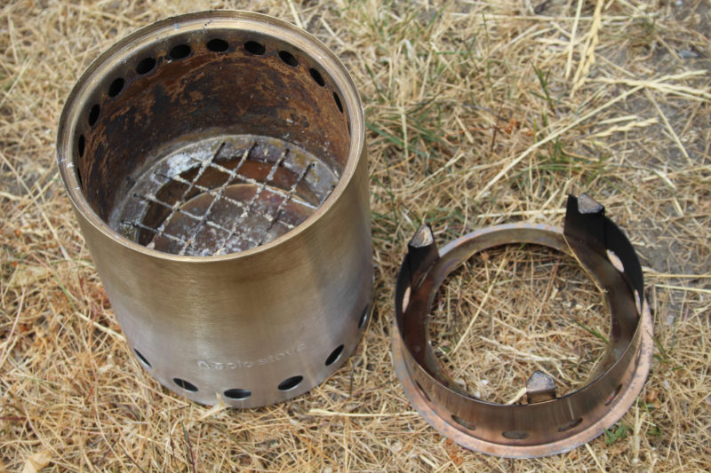 Air enters the stove through the row of holes at the bottom. Half of the air enters the burn chamber through openings hidden beneath the flange supporting the grate; the other half rises between the stove's inner and outer shells, being heated as it goes, and emerges from the row of holes at the top of the burn chamber. The pot support is at right.