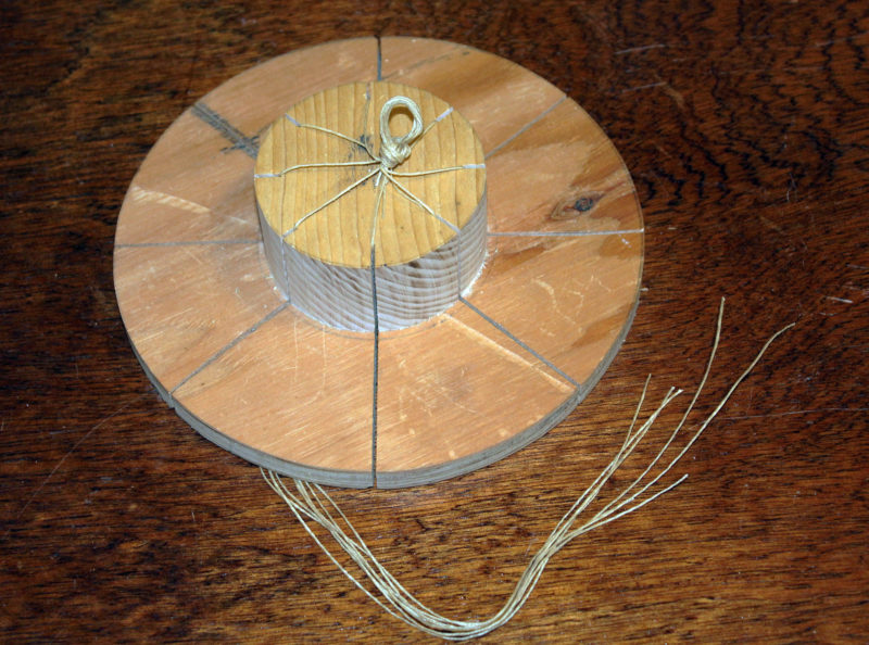I found that I could make the core coils faster and more uniformly by using a jig. I cut a 3” disk cut from 1 ½” stock and fastened it to a 7” plywood disk. Eight bandsaw kerfs accept lengths of marline that will later hold the wraps of the coil together.