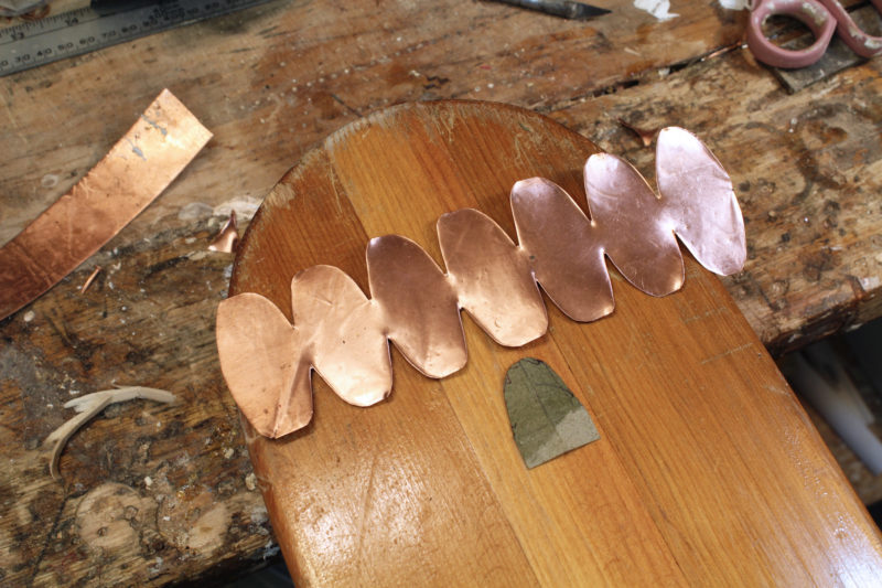 A single tab cut from the pattern and rounded serves as the template for all of the tabs on the copper.