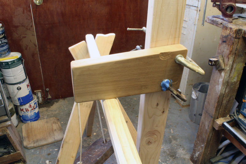 A block of soft red cedar, clamped to a vertical post, provides the downward pressure on the loom.