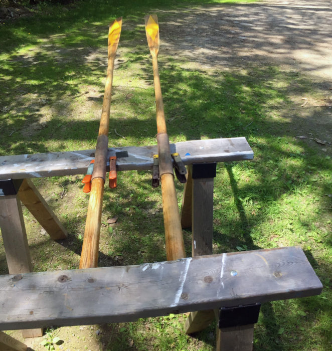 A pair of sawhorses make contact with the handles and the leathers, leaving the rest of the oars free for varnishing.