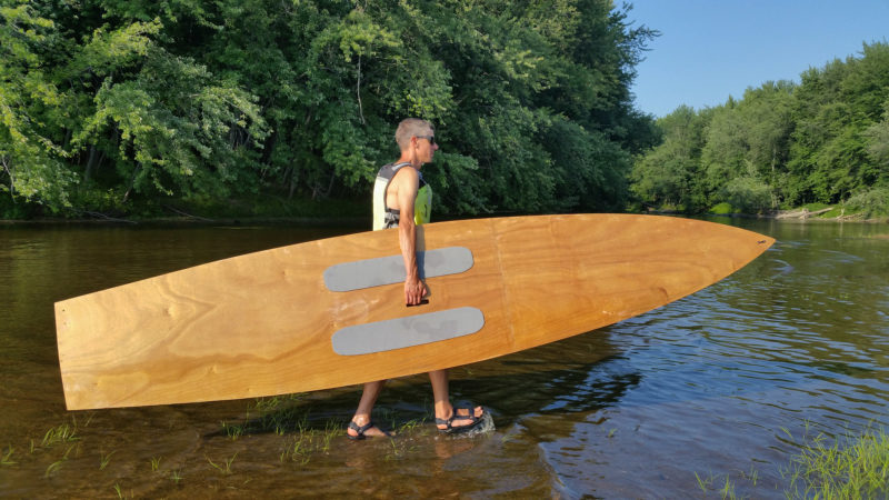 The carry handle is offset to starboard. This tall paddler carries the board with the greater part of the beam under his arm. A paddler with shorter arms would carry the Taal flipped over to put the handle on the high side.