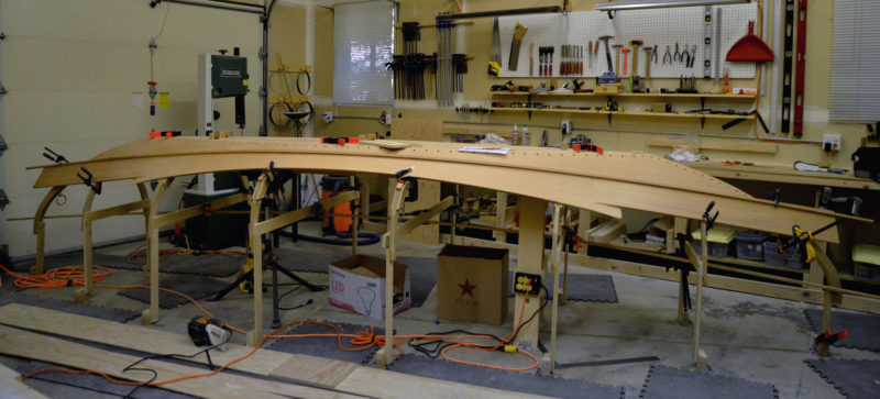 With the garboards in place, a three-piece blank for the broad strake, scarfed and glued, is set on the forms to get the marks for its sheer-side edge. 