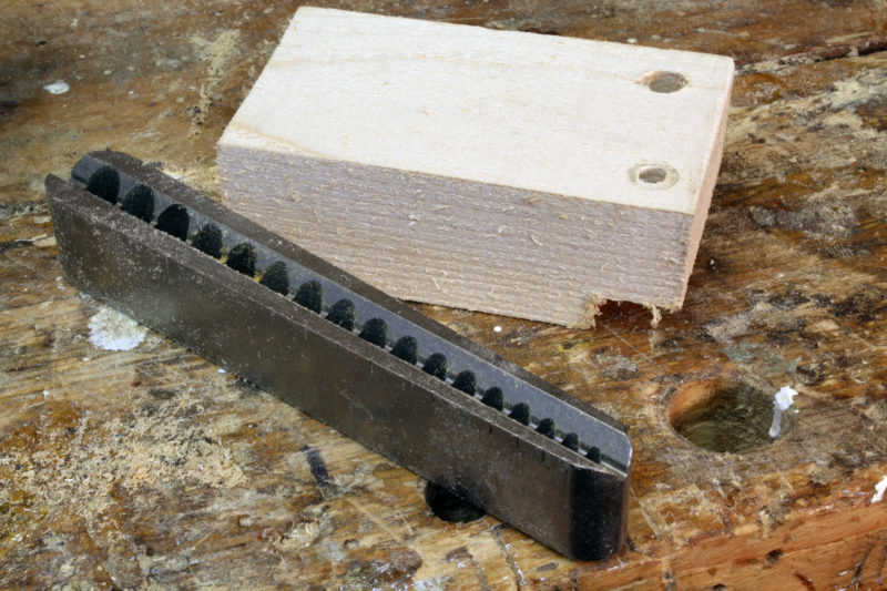 The groove on the bottom straddles corners and cylinders to align the guide. The wooden guide is one I made before buying the V-DrillGuide. Having served its purpose—drilling a single hole for a lag bolt—it's on its way to the fireplace.