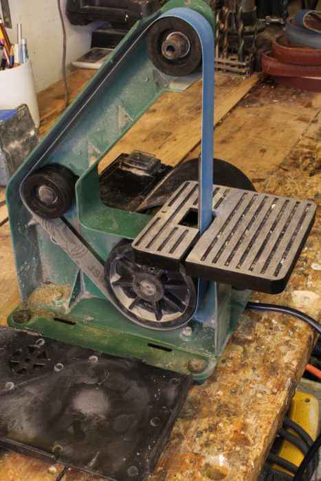 The cover slips off for changing belts. The large drive wheel was out of round but easy enough to fix. The wheel at the back is mounted on a pivot; a spring pushing against he wheel tensions the sanding belt.