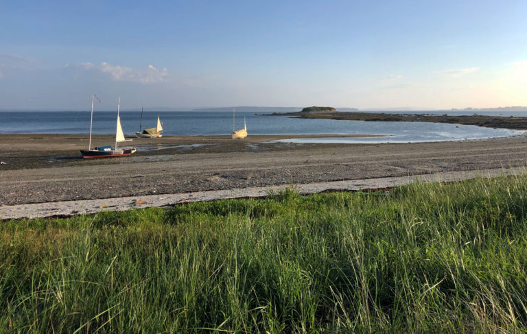 Small sailboats sit on a sandy beach in the morning light.