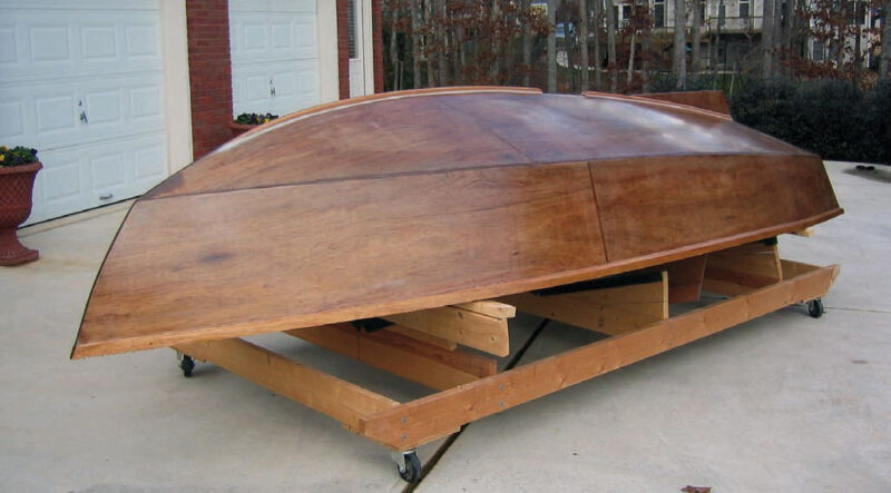 Wooden boat upside down on a rack with rollers.