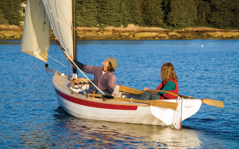 Man adjusts sail aboard a NorseBoat while a woman mans the rudder.