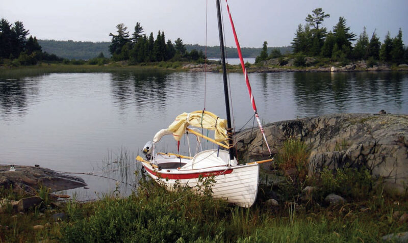 A white NorseBoat sits anchored ashore with the sails down.