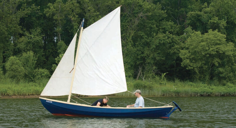 Sailors pilot a blue Marblehead gunning dory with a white sail.