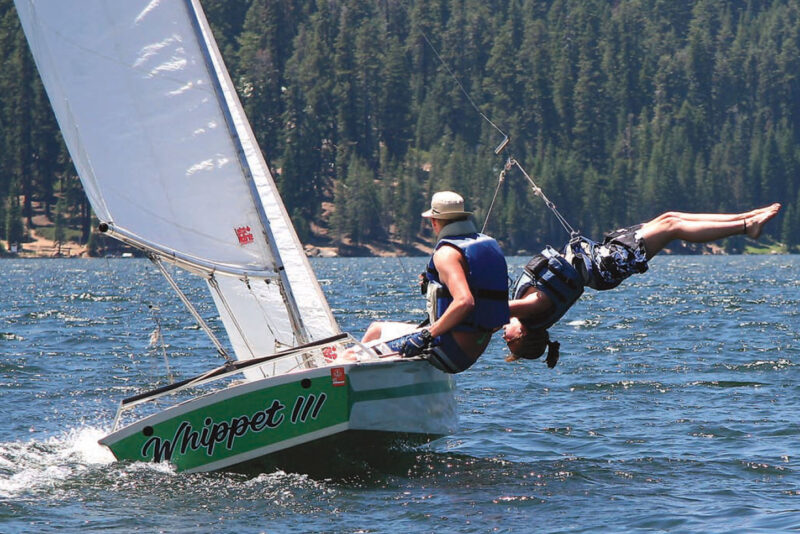 Woman uses trapeze gear aboard a Geary 18 racing dinghy while man pilots the boat.