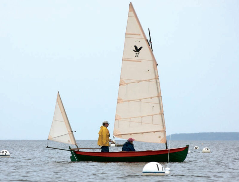 Two sailors aboard the Harrier double-ender with two white sails.