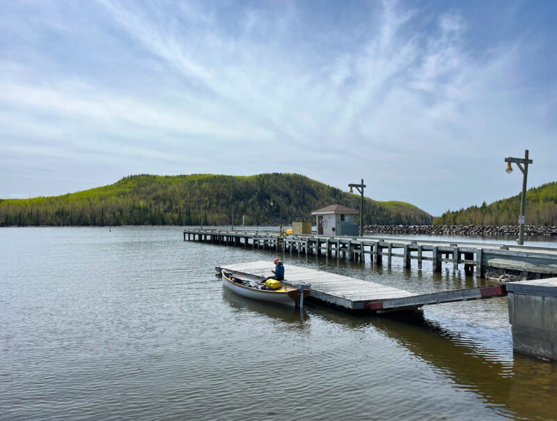 Man sits in a small boat on the water next to a dock.