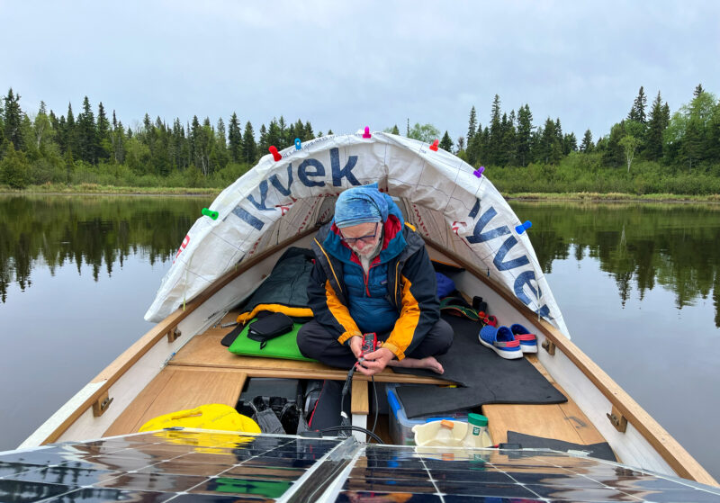 Man sits cross-legged on a boat under a Tyvek tent and checks solar panels.