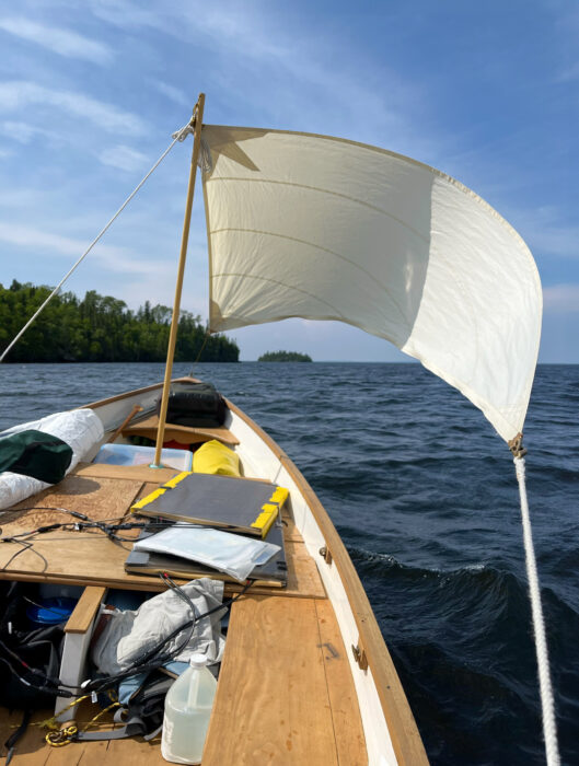 Small white sail on a wooden boat loaded with gear.