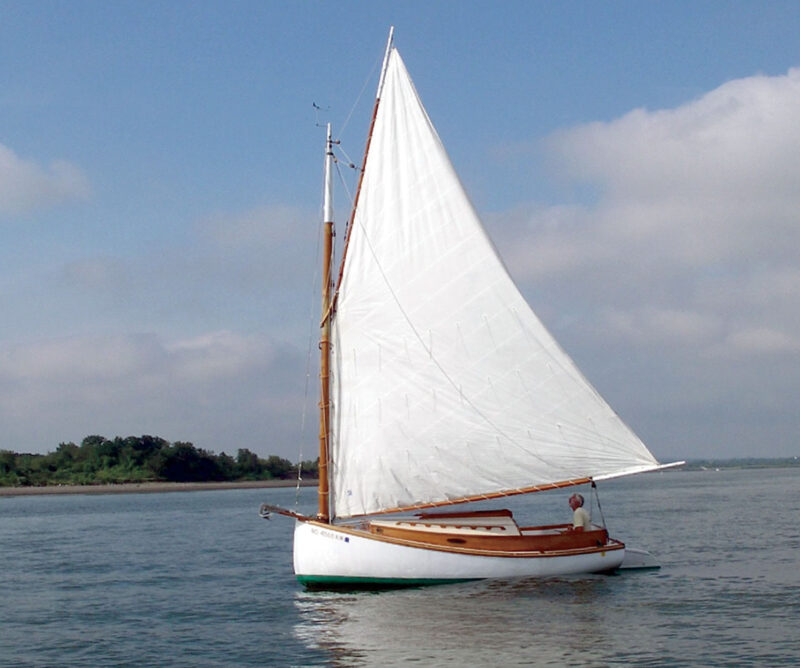 Man sailing Fenwick Williams catboat with white sail.