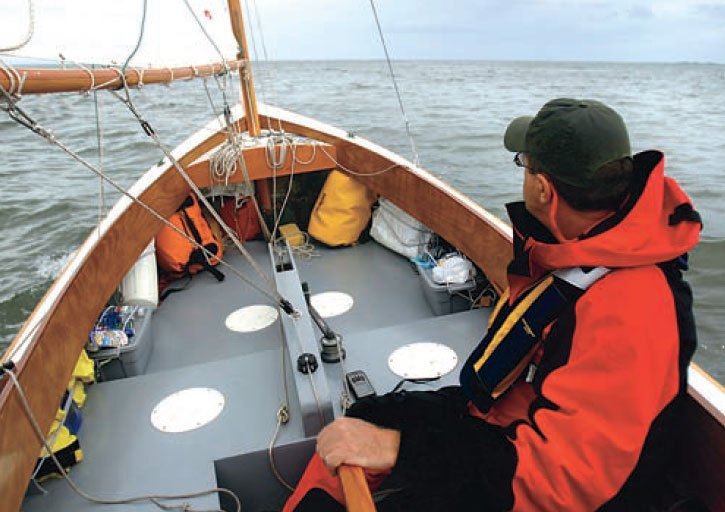 Man wearing a ball cap steers a sailboat.