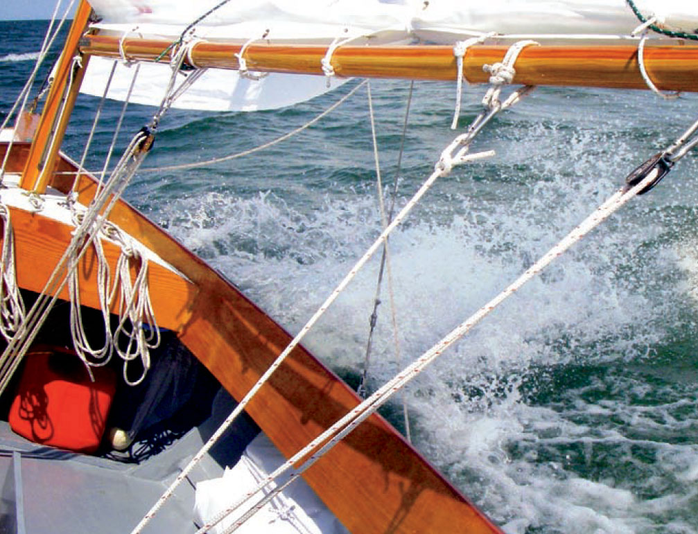 Ocean water sprays the hull of a Pathfinder yawl.