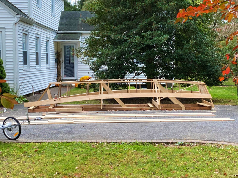 A partially finished hull of a United Nations Flat-Bottomed Skiff sits in a driveway.