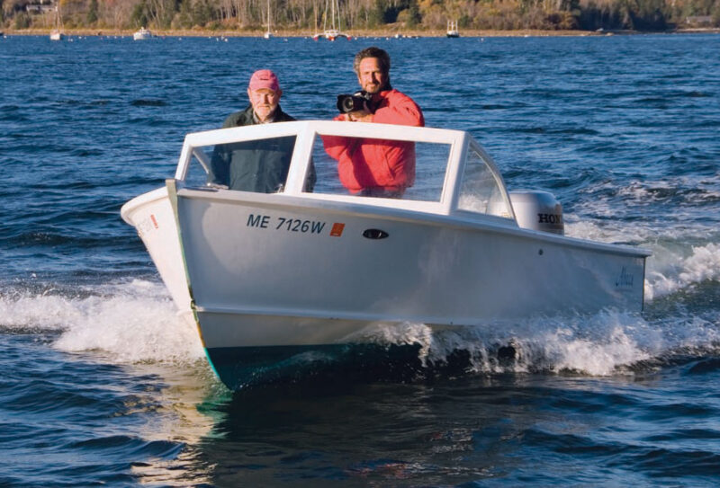 Man pilots an Albury runabout while another takes pictures with a camera.