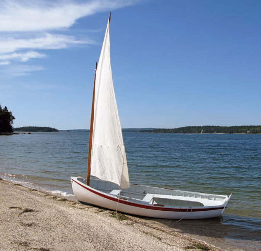 White Catspaw dinghy with a white sail sits ashore.