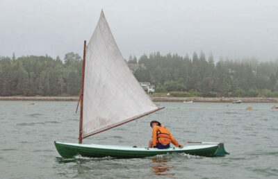 Man in orange jacket pilots a Delaware Ducker sailboat.