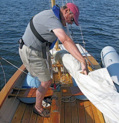 Man furls a white mizzen sail aboard a Coquina yacht.