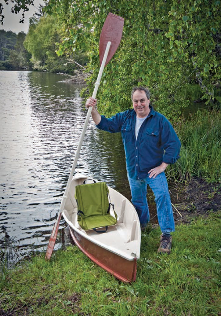 Man stands next to NEWT canoe on the shore holding a double paddle.