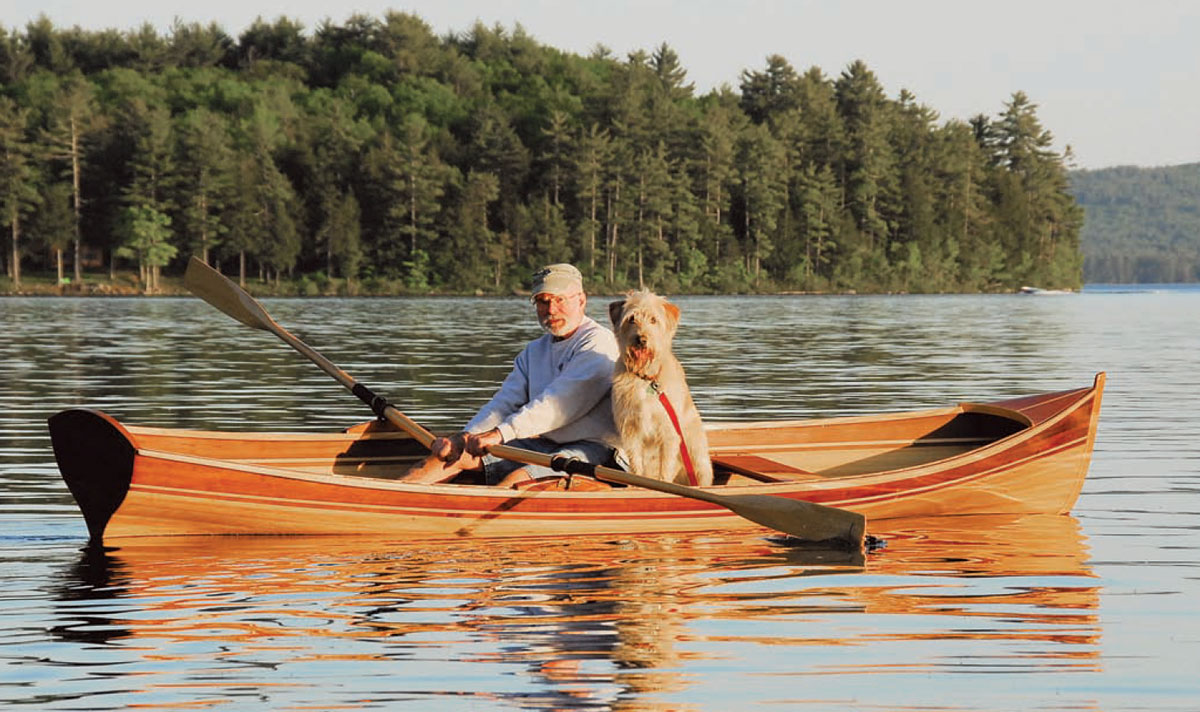 Man paddling a Newfound Rangeley boat with a dog sitting beside him.