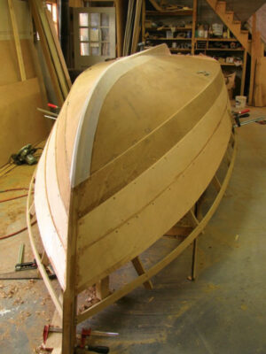 Partially finished plywood boat hull sits upside down in a shop.