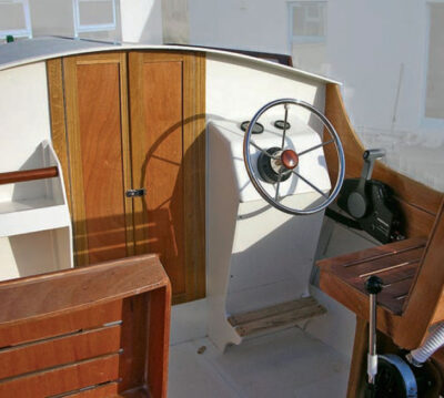 View of a boat's cockpit with chrome steering wheel and wooden seats.