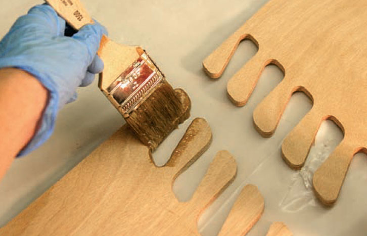 Photo of hand using brush to apply epoxy to wood strakes.