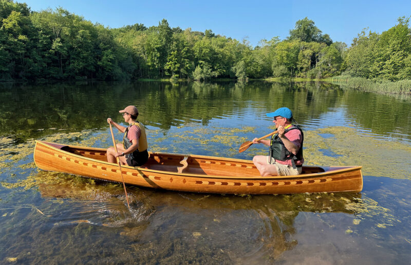 Two people paddling strip-planked canoe