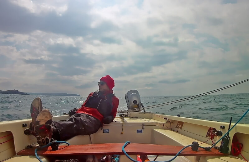 Man relaxing in sailboat going downwind with self-steering mechanism