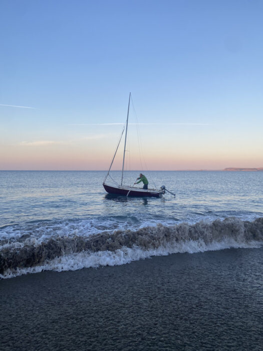 Man paddling sailboat away from beach surf