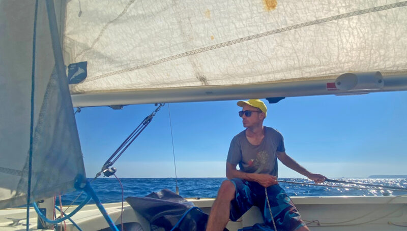 Man singlehanding small sailboat on sunny day
