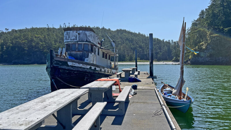 Dory and derelict fishing boat alongside wooden dock in Bowman Bay
