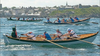 Five-person crew rows a racing skiff with two more boats in the background