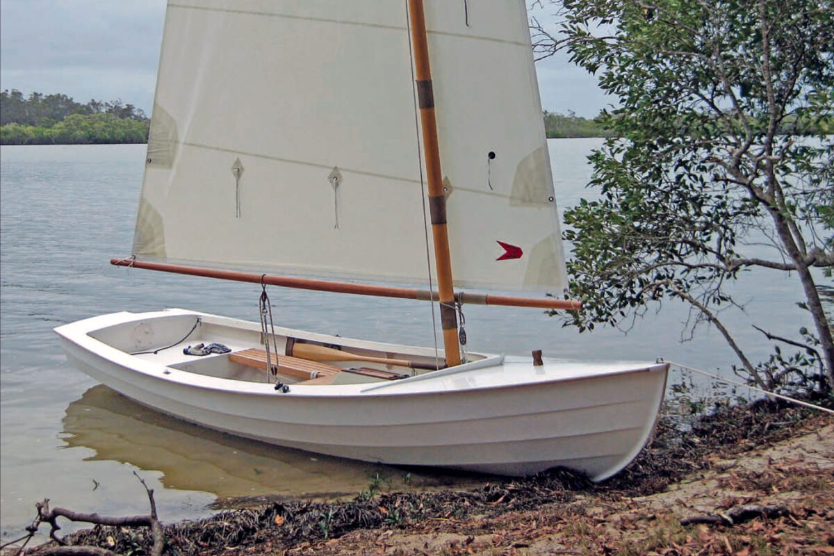 Small white Phoenix III sailboat sits moored along a sandy shoreline in the water.