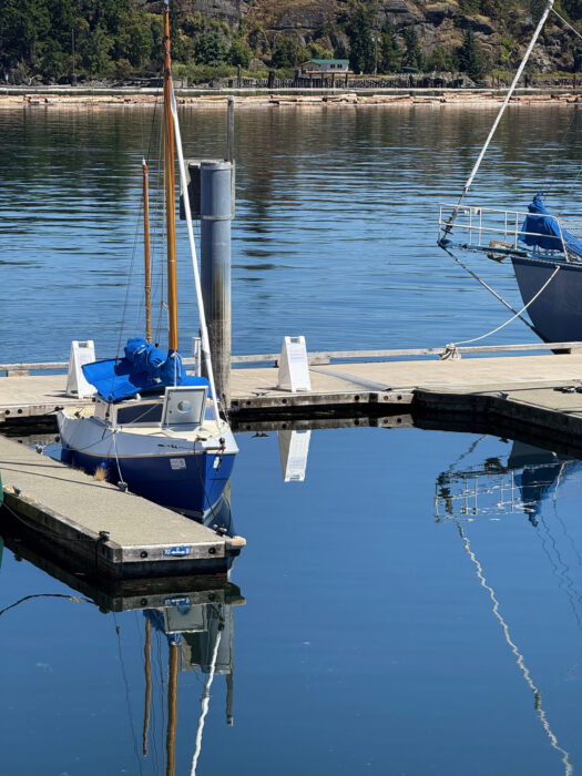 Two-masted sailboat alongside float in calm-water marina.