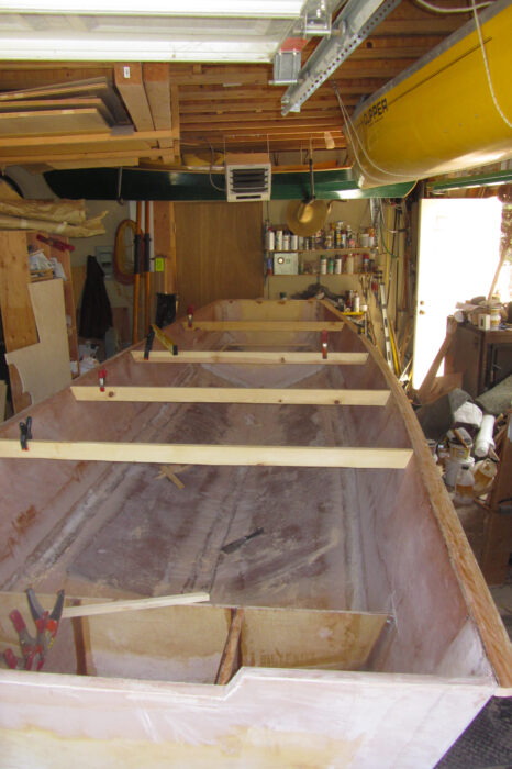 Plywood stitch-and-glue boat under construction in cramped workshop.