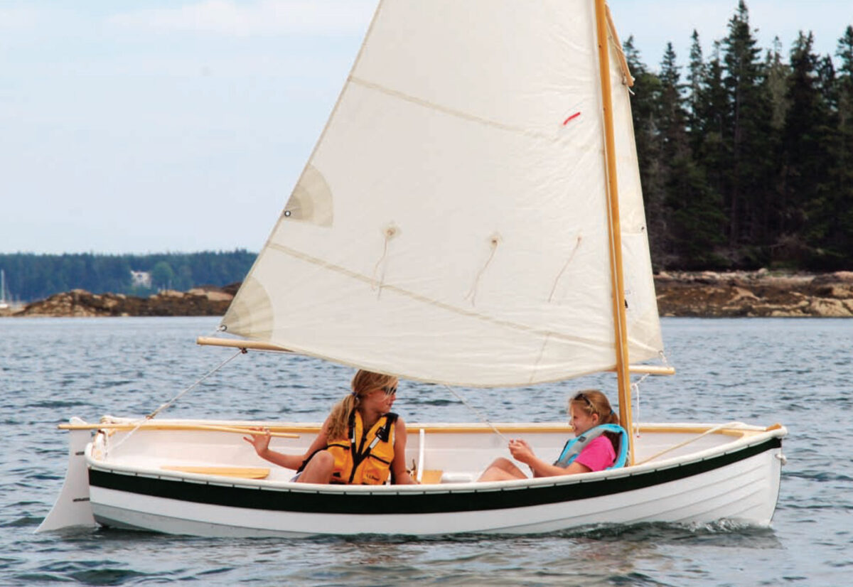 Two young girls wearing lifevests ride aboard a small white sailboat.