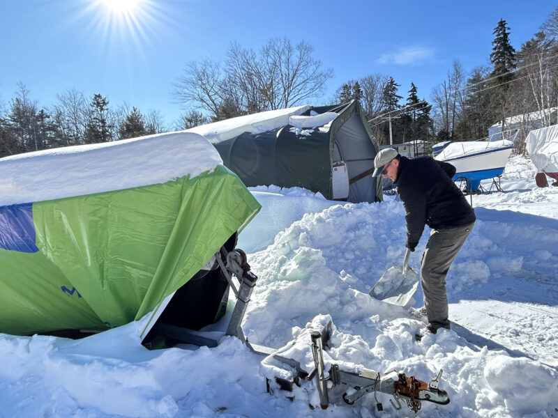 Man shoveling snow away from a tarp-covered Rhodes 18
